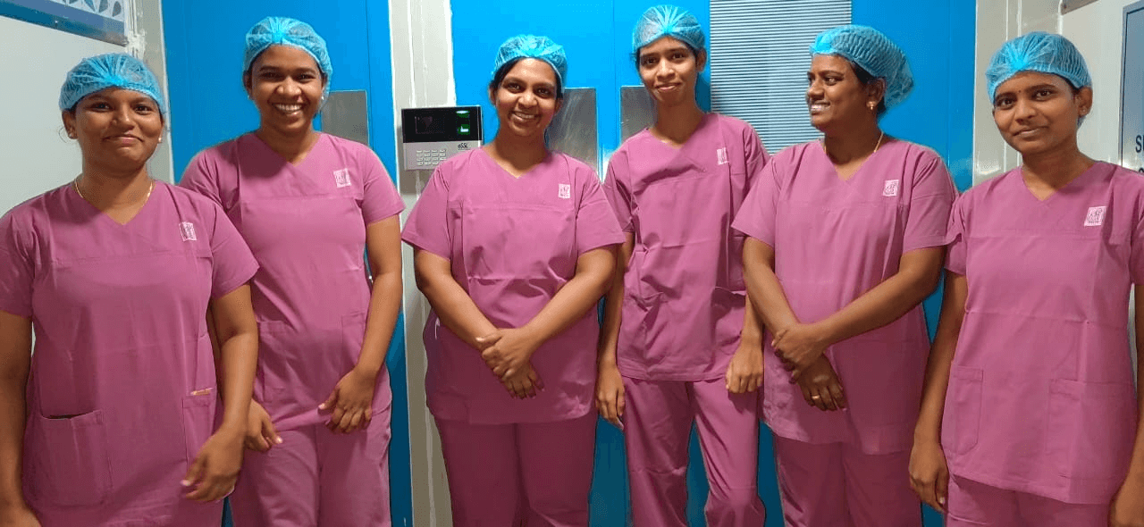 Six smiling female medical staff in pink scrubs and blue hairnets.