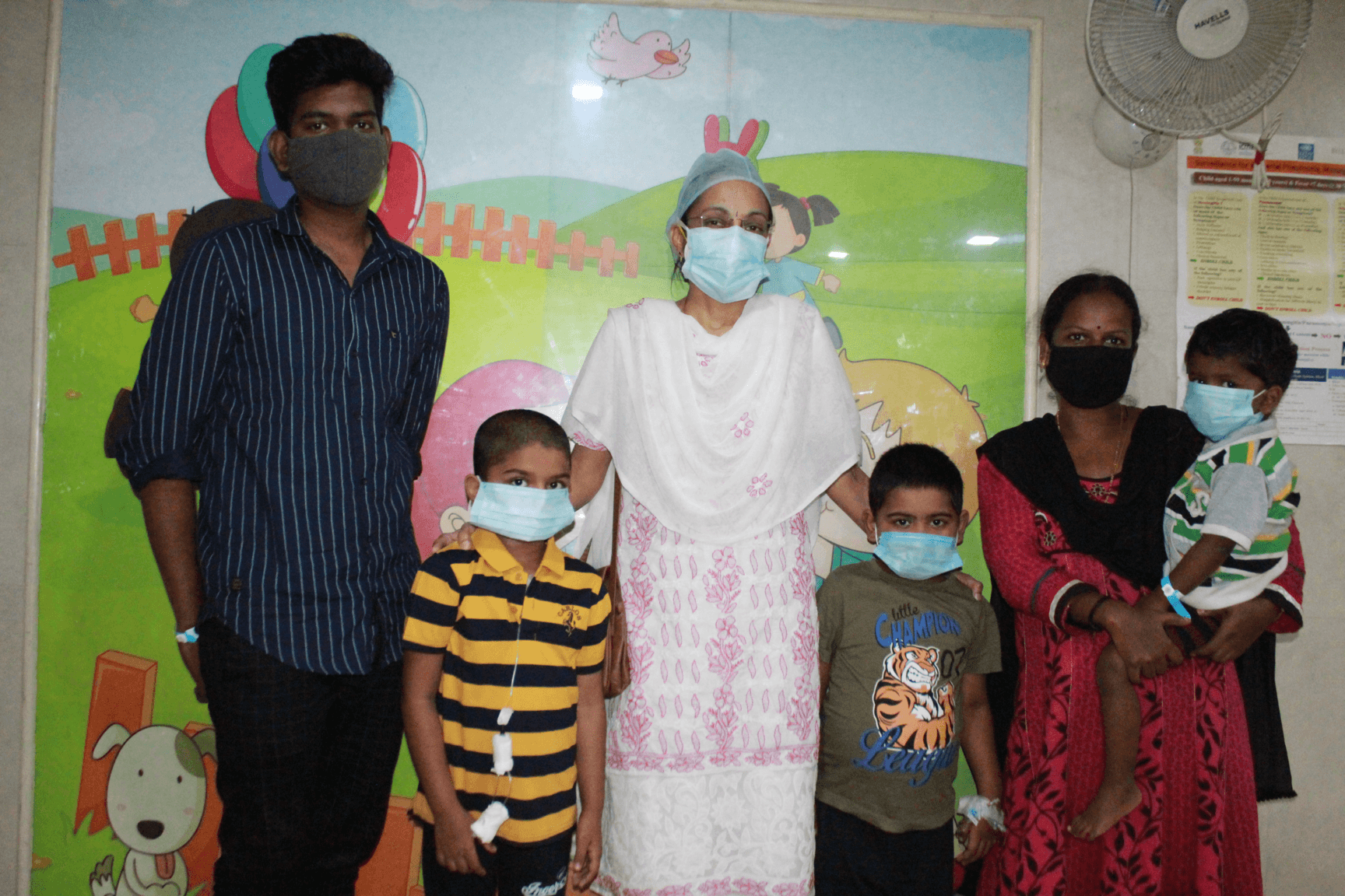 Doctor and adults with three masked boys in front of a colorful mural.