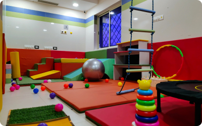 Colorful pediatric therapy playroom equipped with soft mats, toys, and climbing structures.