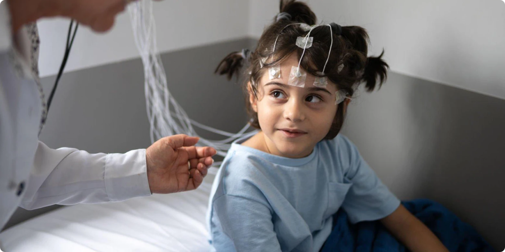 A medical professional attends to a young child with electrodes attached to their head for a medical test.